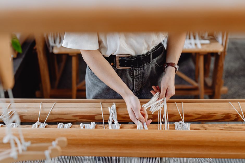 Close-up of hands weaving on a traditional wooden loom in a workshop.